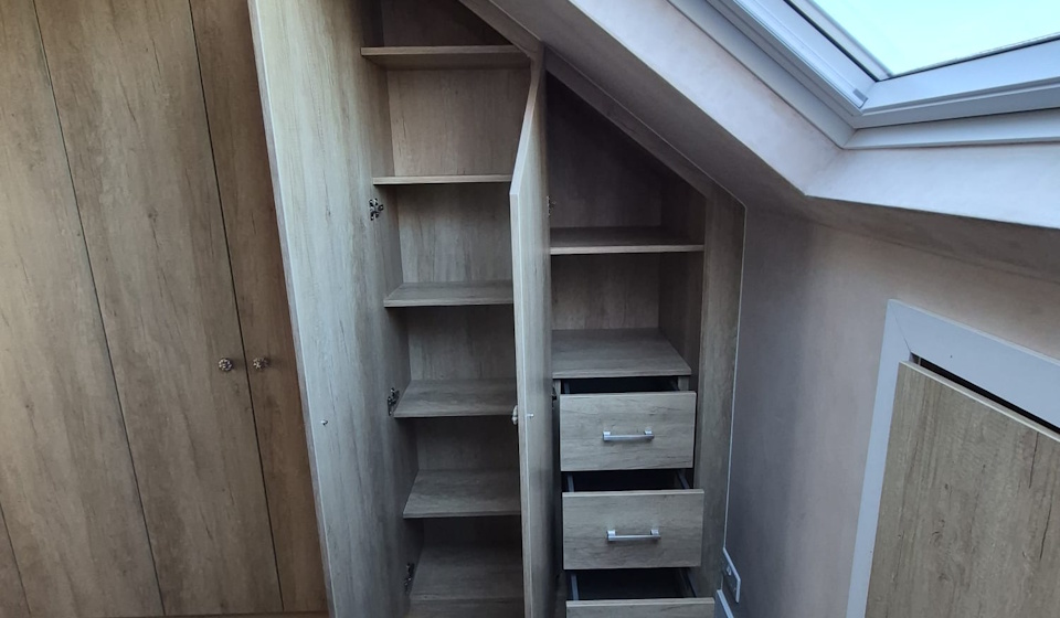 Light oak fitted wardrobes under a sloping ceiling, with doors open to show shelving and internal drawers