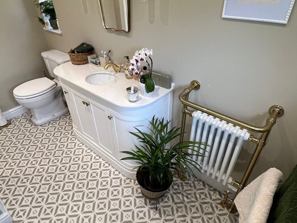 Curved white vanity with brass taps, wall lights and patterned floor tiles