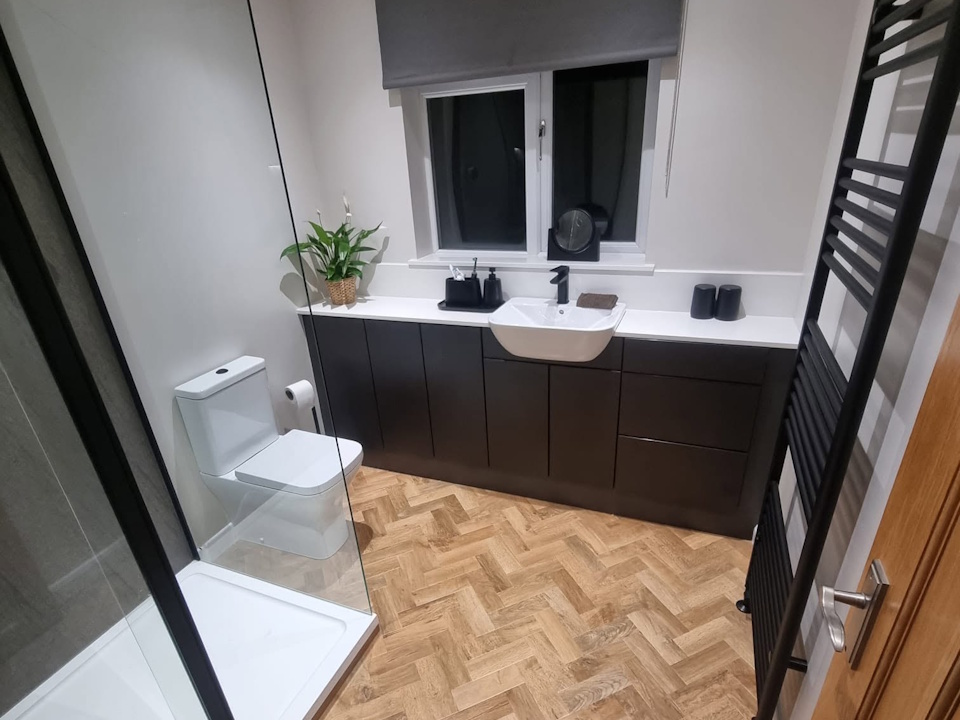 Bathroom with dark handleless vanity units, quartz worktop and herringbone floor