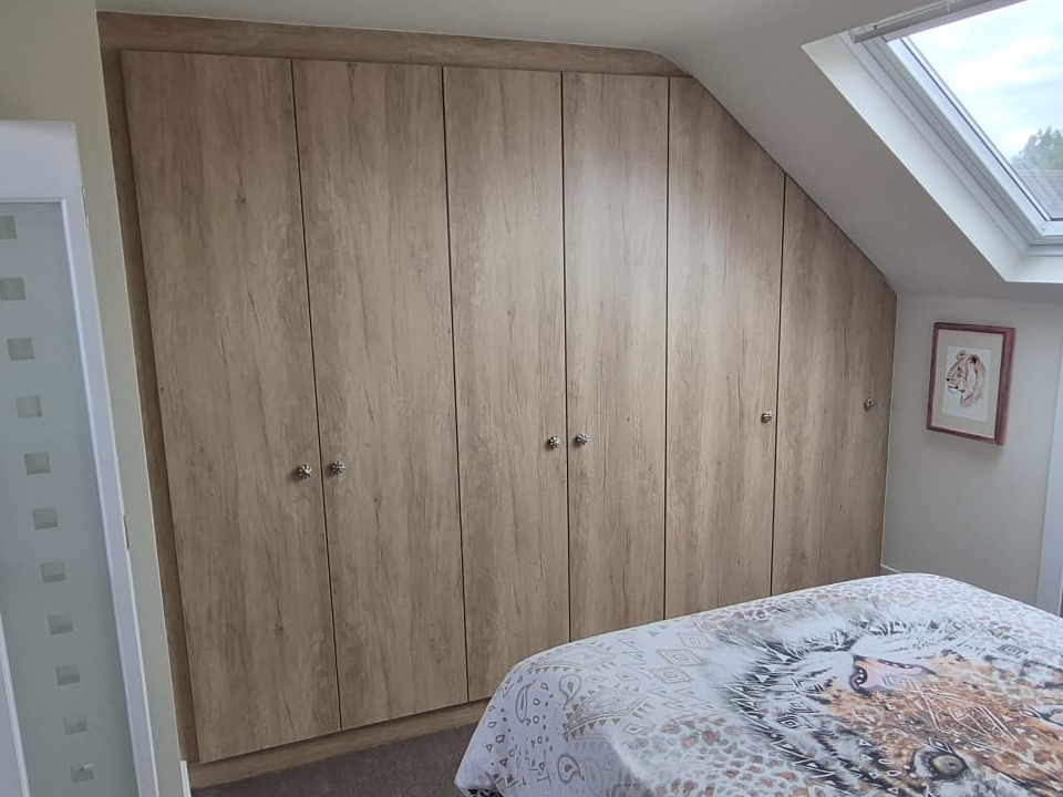 Light oak loft wardrobes with doors angled to follow the sloping ceiling