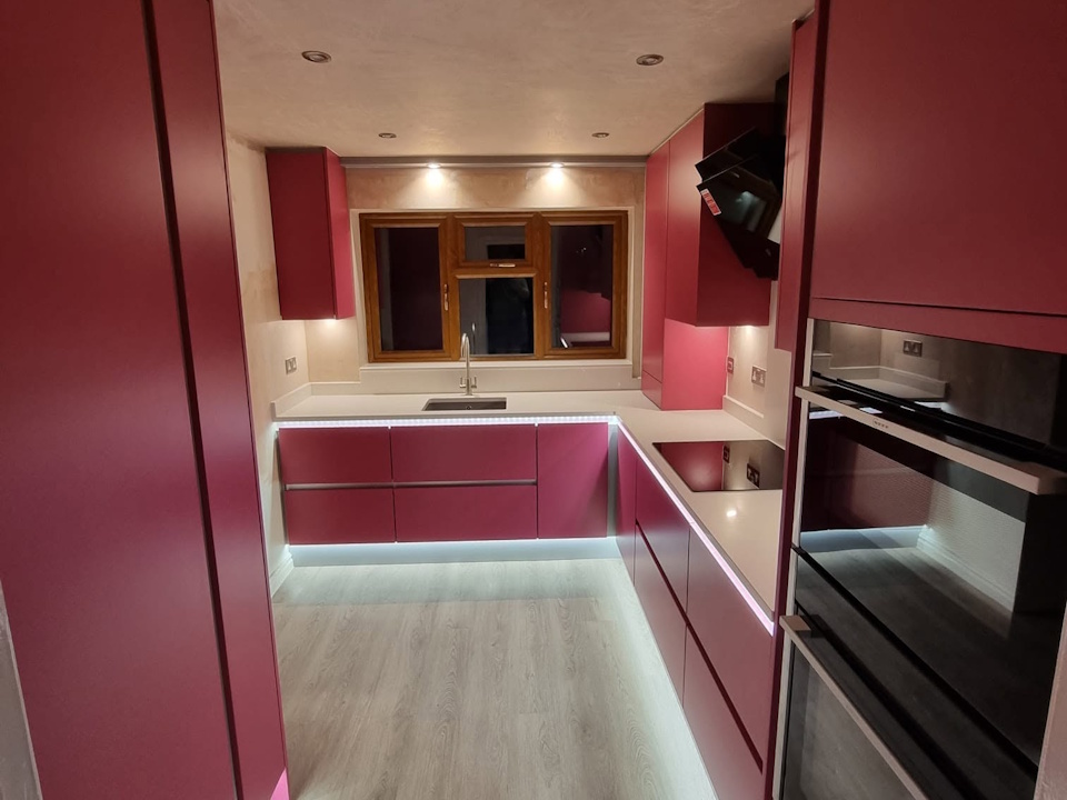 Raspberry handleless kitchen with white quartz worktops and LED plinth lighting
